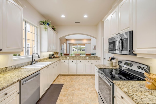 3145 Connemara Dr, Ormond Beach, FL 32174 - kitchen featuring stainless steel appliances, a sink, arched walkways, light stone countertops, and white cabinetry