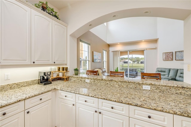 3145 Connemara Dr, Ormond Beach, FL 32174 - kitchen featuring arched walkways, light stone counters, white cabinets, and open floor plan
