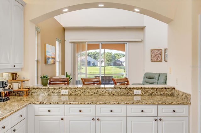 3145 Connemara Dr, Ormond Beach, FL 32174 - kitchen with arched walkways, light stone countertops, and white cabinetry