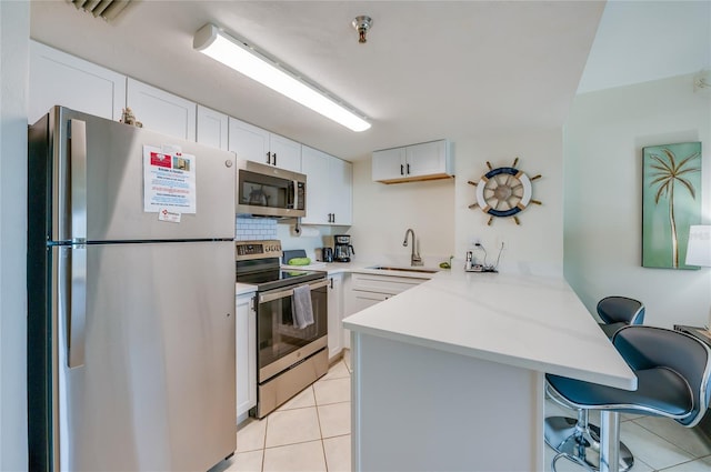 kitchen featuring a peninsula, light countertops, a breakfast bar area, appliances with stainless steel finishes, and a sink