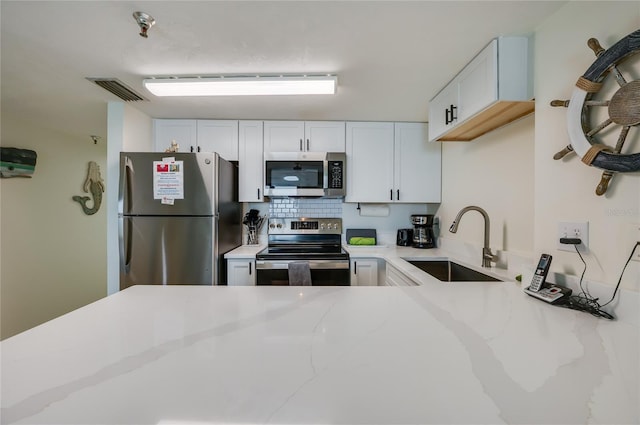 kitchen featuring tasteful backsplash, white cabinets, a sink, appliances with stainless steel finishes, and light stone counters