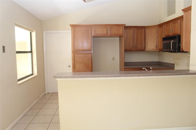 kitchen featuring light tile patterned floors, lofted ceiling, a peninsula, black microwave, and brown cabinets