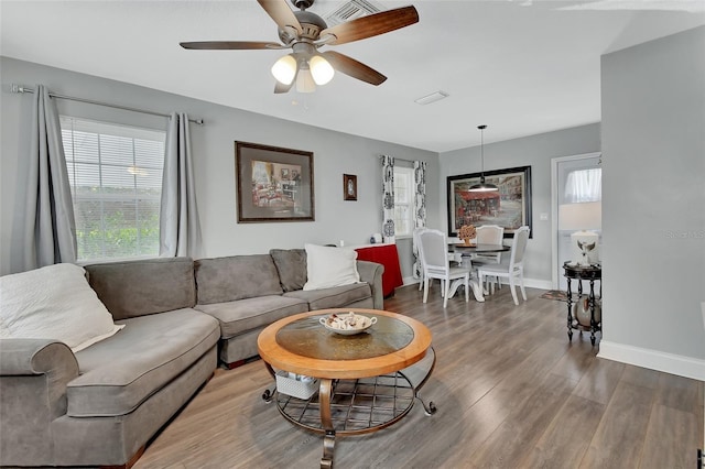 living area featuring a ceiling fan, visible vents, baseboards, and wood finished floors