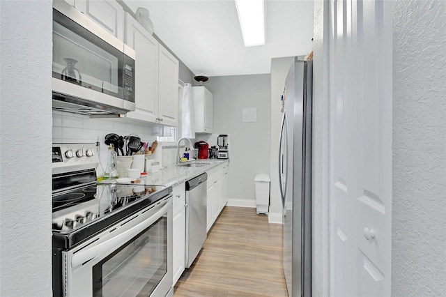 kitchen with a sink, white cabinetry, light wood-style flooring, stainless steel appliances, and decorative backsplash