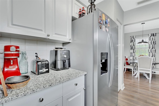 kitchen featuring white cabinets, visible vents, stainless steel fridge, light wood-style floors, and backsplash