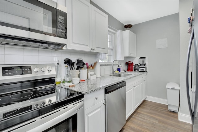 kitchen featuring light wood finished floors, tasteful backsplash, appliances with stainless steel finishes, white cabinetry, and a sink