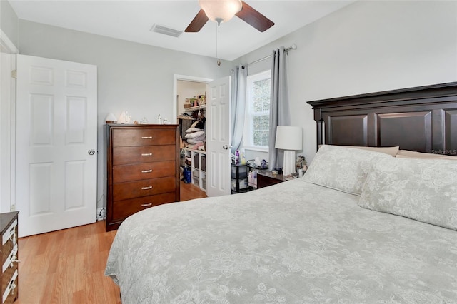 bedroom featuring a spacious closet, light wood finished floors, ceiling fan, visible vents, and a closet