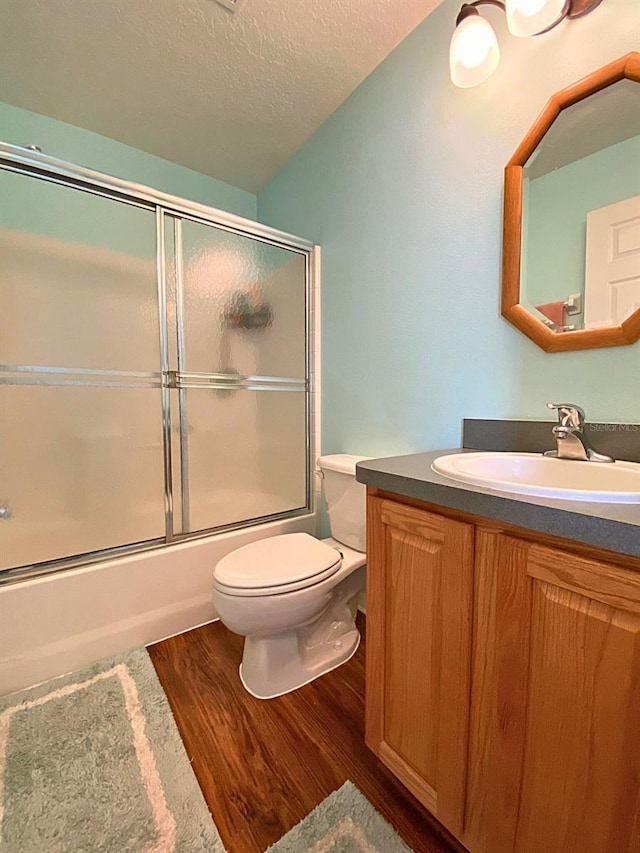 full bathroom featuring a textured ceiling, wood finished floors, toilet, vanity, and shower / bath combination with glass door