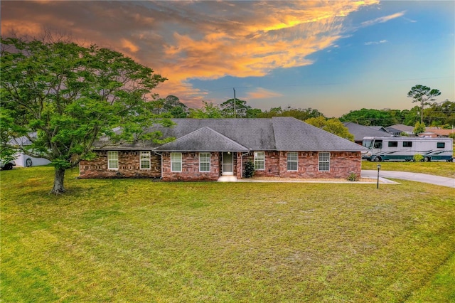 ranch-style house with stone siding, concrete driveway, a shingled roof, and a lawn