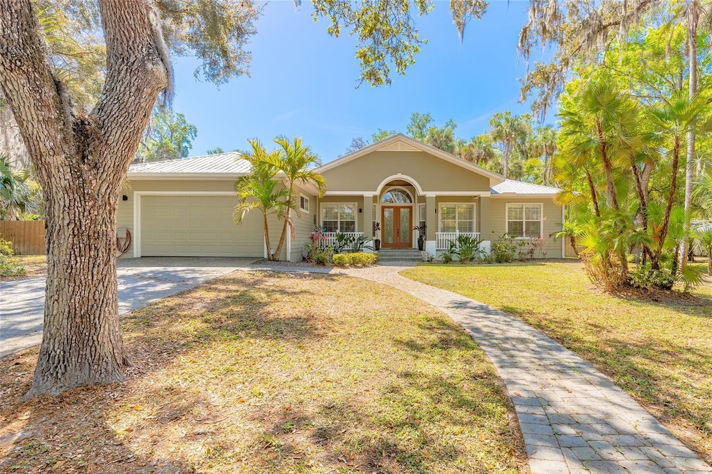 2646 Turnbull Bay Rd, New Smyrna Beach, FL 32168 - ranch-style house with driveway, french doors, a front lawn, metal roof, and a garage