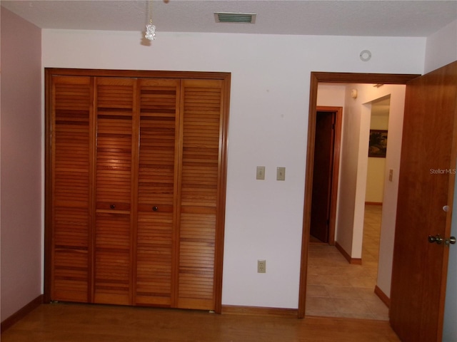 unfurnished bedroom featuring a closet, a textured ceiling, visible vents, baseboards, and light wood-type flooring