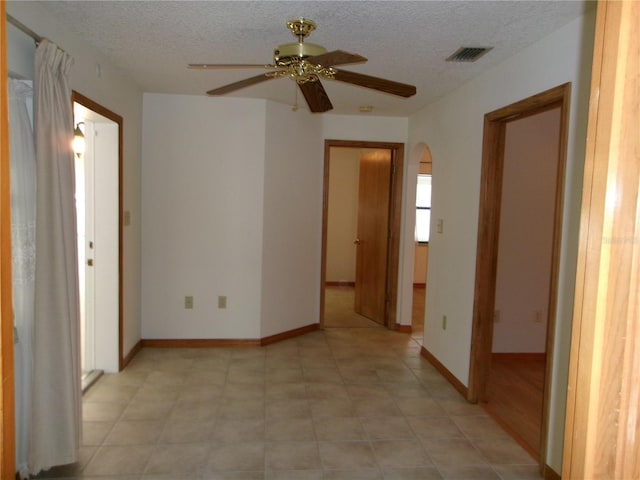 spare room featuring a textured ceiling, visible vents, baseboards, a ceiling fan, and arched walkways