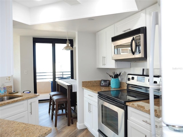 kitchen featuring stainless steel appliances, light stone counters, white cabinetry, and light wood-style flooring