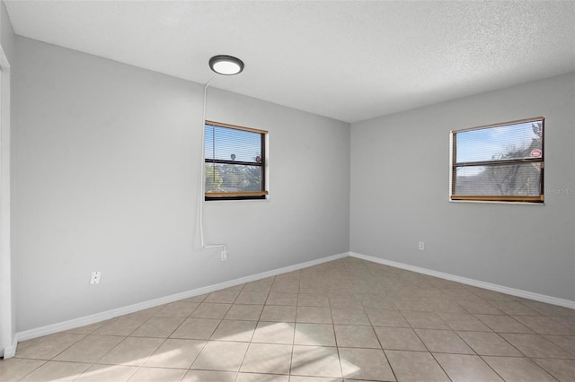 spare room featuring baseboards, a textured ceiling, and light tile patterned floors