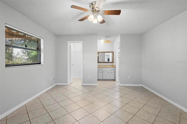 empty room with light tile patterned floors, baseboards, a textured ceiling, and ceiling fan