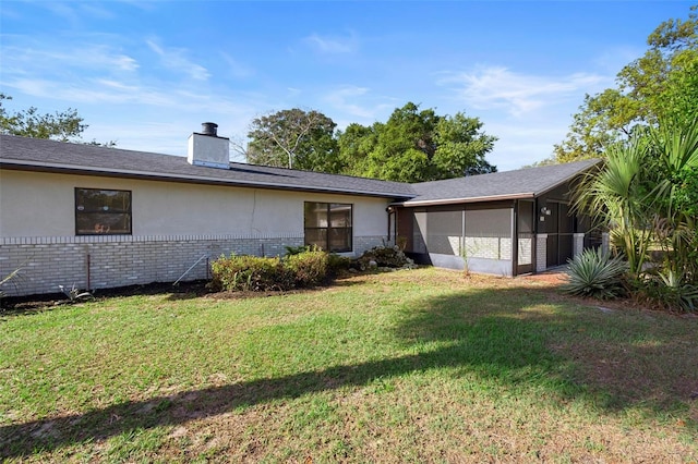 ranch-style home featuring a front lawn, a chimney, brick siding, a sunroom, and stucco siding