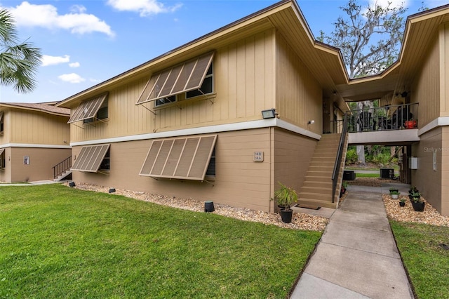view of side of home featuring cooling unit, a yard, and stairway