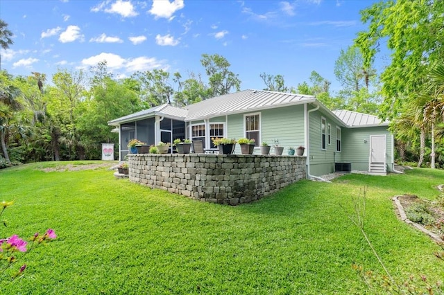 rear view of house featuring a sunroom, entry steps, metal roof, a lawn, and a standing seam roof