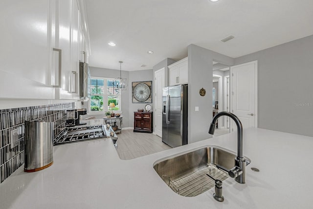 kitchen featuring stainless steel fridge with ice dispenser, decorative light fixtures, a sink, light countertops, and white cabinetry