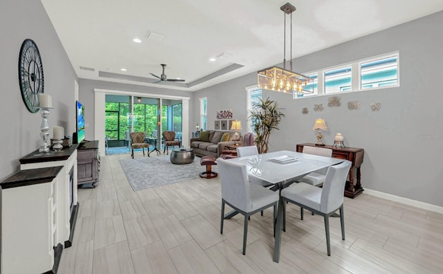 dining space with baseboards, recessed lighting, visible vents, a tray ceiling, and ceiling fan with notable chandelier