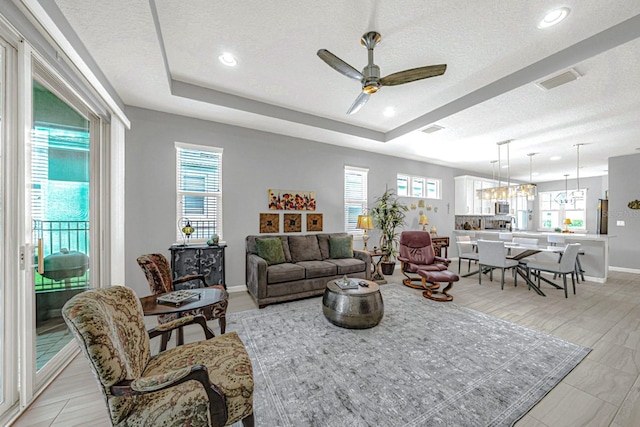 living area with a tray ceiling, a wealth of natural light, and a ceiling fan