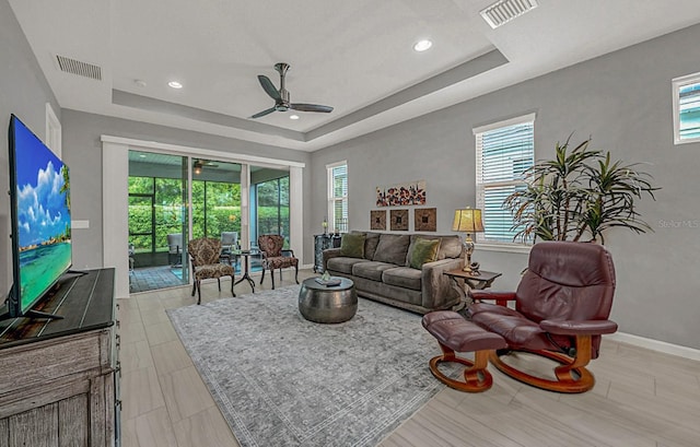 living room with a tray ceiling, a ceiling fan, visible vents, and plenty of natural light