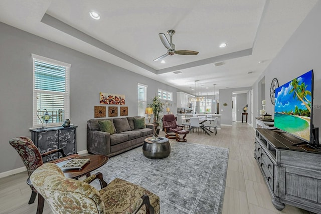 living area with a raised ceiling, baseboards, a ceiling fan, and recessed lighting