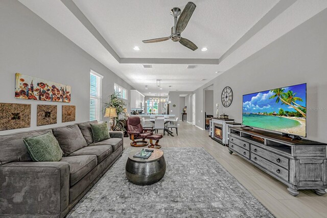 living area with light wood-type flooring, recessed lighting, visible vents, a tray ceiling, and ceiling fan with notable chandelier