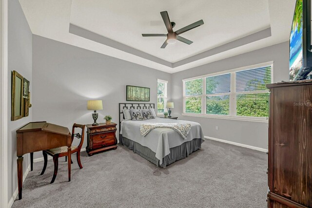 bedroom featuring light carpet, ceiling fan, baseboards, and a raised ceiling