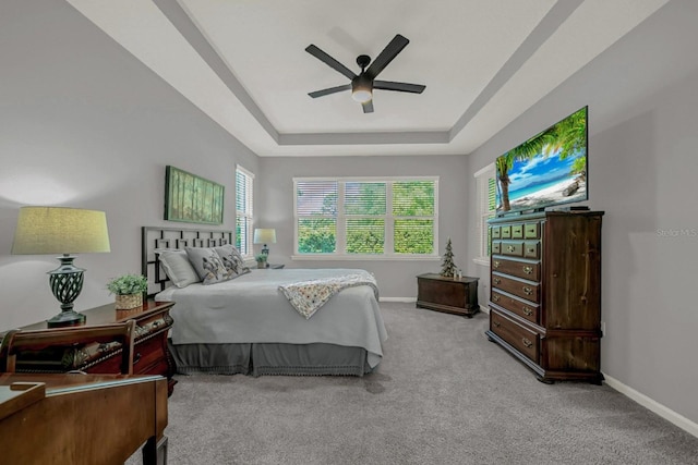 bedroom featuring baseboards, a raised ceiling, light colored carpet, and a ceiling fan