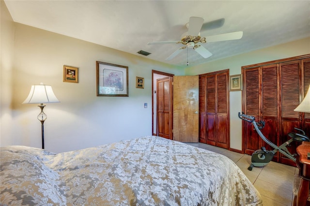 bedroom with light tile patterned flooring, two closets, visible vents, and ceiling fan