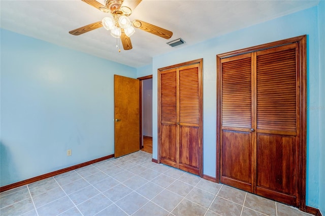 unfurnished bedroom featuring light tile patterned flooring, baseboards, visible vents, a ceiling fan, and multiple closets