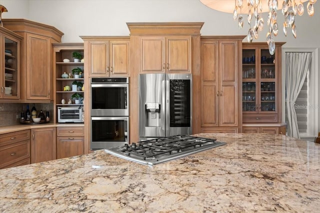 3310 John Anderson Dr, Ormond Beach, FL 32176 - kitchen with light stone counters, a chandelier, glass insert cabinets, open shelves, and appliances with stainless steel finishes