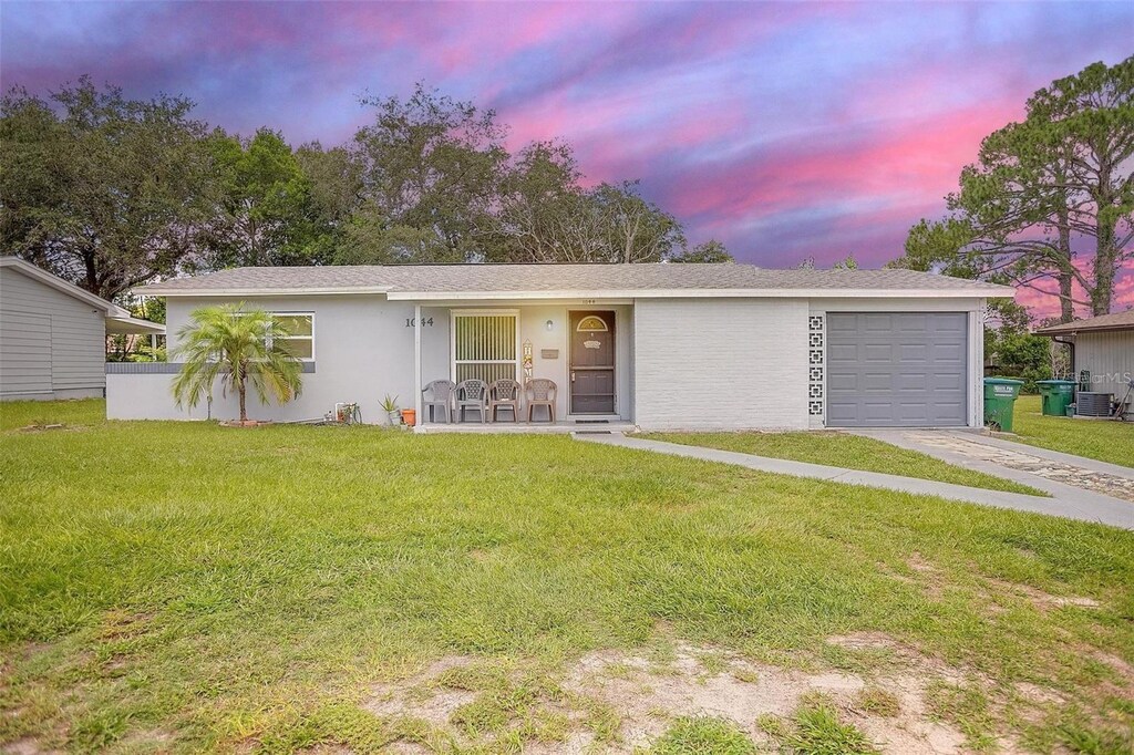 1044 Deltona Blvd, Deltona, FL 32725 - single story home with concrete driveway, stucco siding, an attached garage, central AC, and a yard