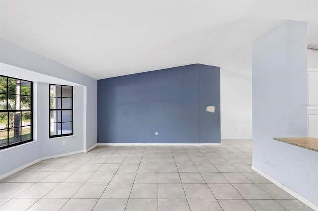 empty room featuring light tile patterned floors, baseboards, and lofted ceiling