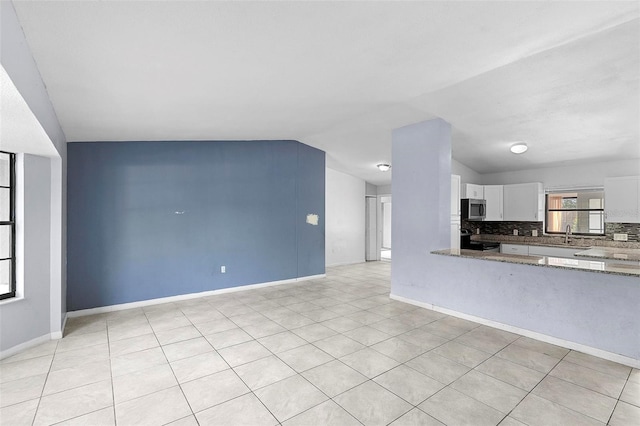 unfurnished living room with light tile patterned floors, baseboards, a sink, and lofted ceiling