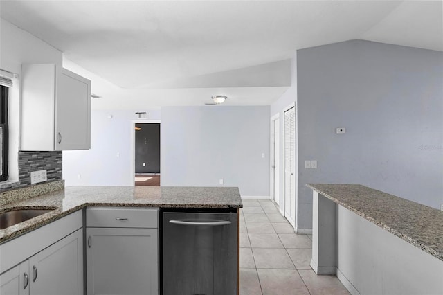 kitchen with vaulted ceiling, a peninsula, light tile patterned floors, light stone countertops, and decorative backsplash