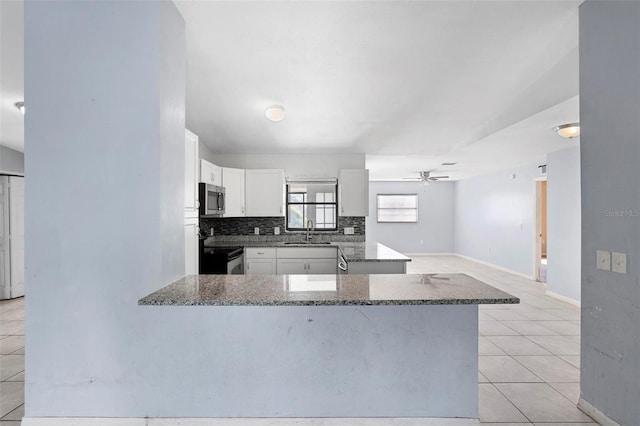 kitchen featuring a peninsula, white cabinetry, dark stone counters, stainless steel appliances, and a sink