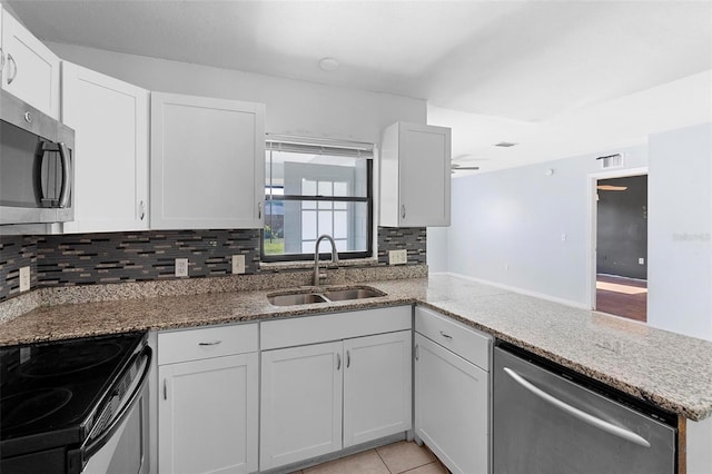 kitchen featuring appliances with stainless steel finishes, a peninsula, light stone countertops, decorative backsplash, and a sink