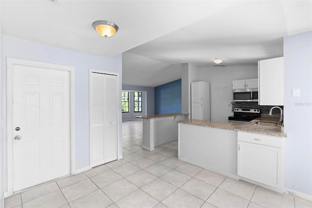 kitchen featuring a sink, a peninsula, white cabinetry, vaulted ceiling, and stainless steel appliances