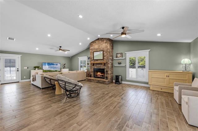 living room featuring light wood finished floors, ceiling fan, a stone fireplace, and visible vents