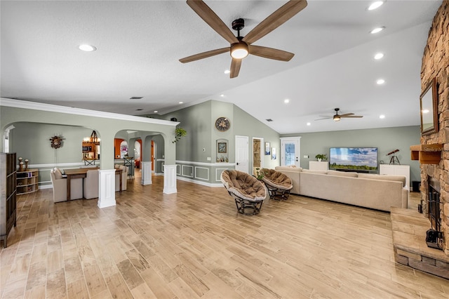 living area with arched walkways, a stone fireplace, a ceiling fan, light wood-style flooring, and lofted ceiling