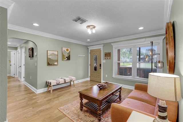 living room with visible vents, baseboards, arched walkways, ornamental molding, and light wood-type flooring