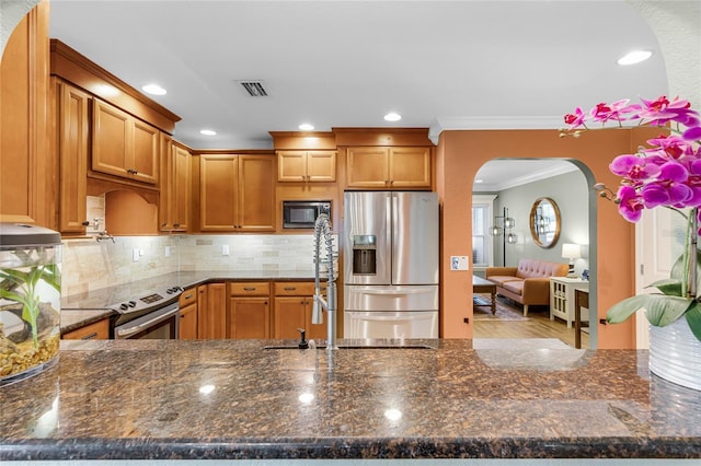 kitchen with crown molding, visible vents, dark stone counters, appliances with stainless steel finishes, and arched walkways