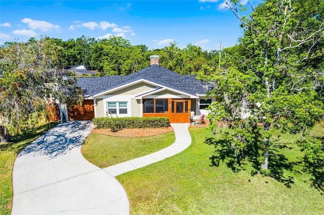 bungalow with concrete driveway, roof with shingles, a chimney, and a front lawn