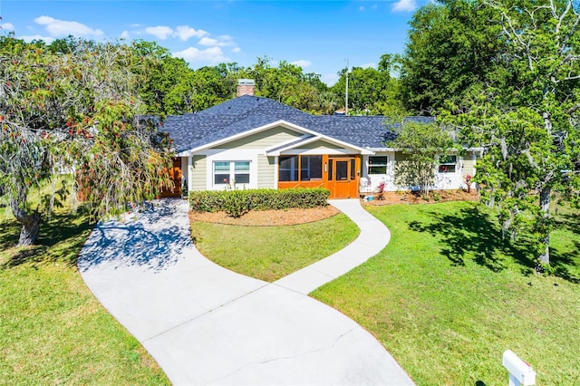 view of front of home with a front yard, roof with shingles, driveway, and a chimney
