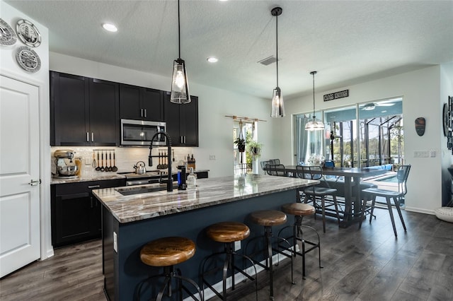 kitchen featuring visible vents, a sink, dark wood-style flooring, stainless steel microwave, and backsplash
