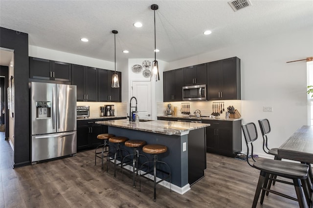 kitchen with appliances with stainless steel finishes, light stone counters, visible vents, dark wood finished floors, and a sink