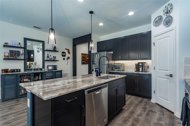 kitchen with visible vents, open shelves, a sink, a center island with sink, and stainless steel appliances