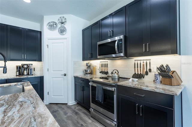 kitchen featuring tasteful backsplash, light stone counters, dark wood-style floors, appliances with stainless steel finishes, and a sink